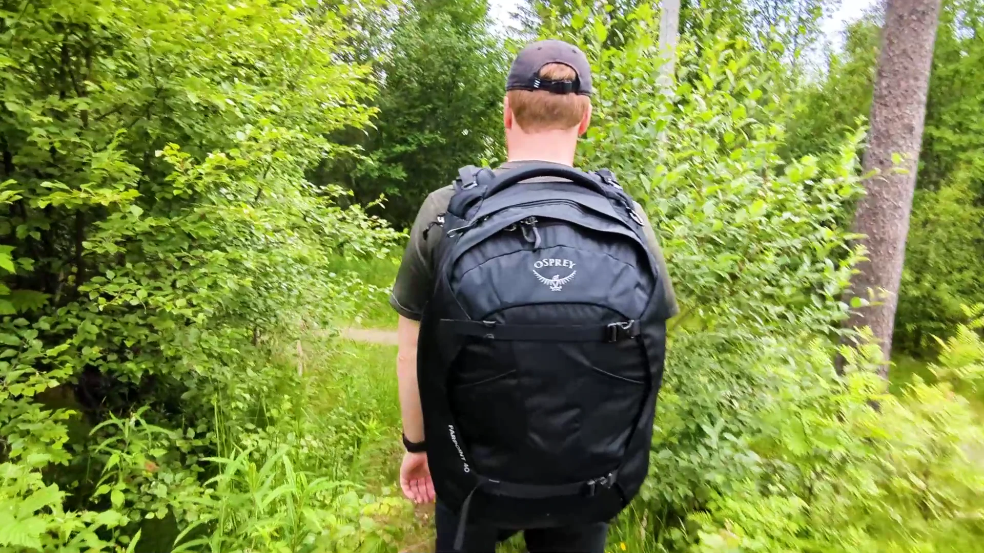 Person hiking through a lush green forest trail wearing the Osprey Farpoint 40