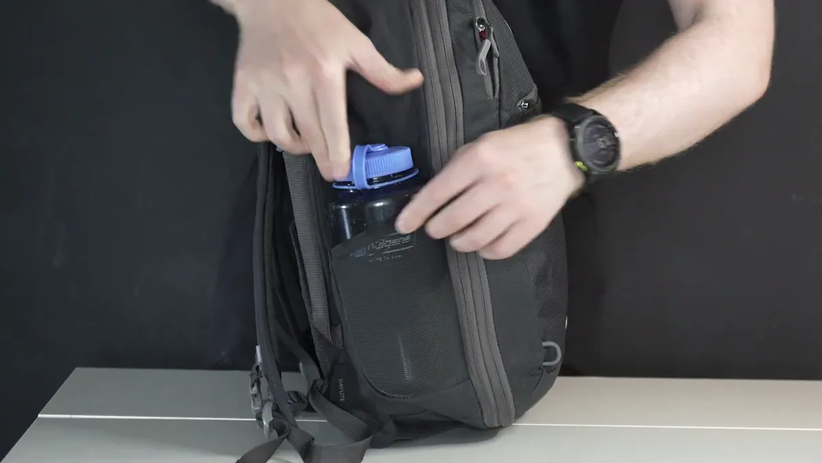 A one-litre Nalgene bottle being slid into the stretch mesh side pocket of the Osprey Daylite 26+6