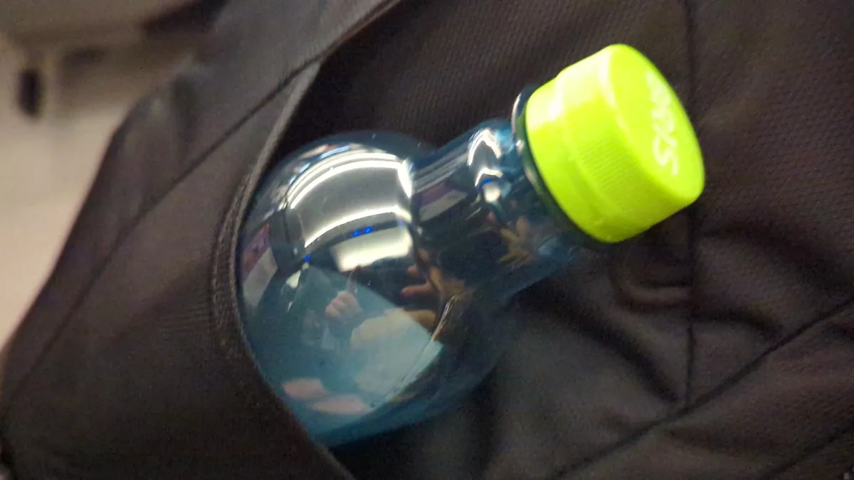 A clear water bottle with a green cap tucked into the front shove-it pocket of the Osprey Farpoint 40.